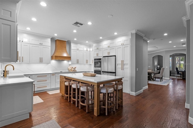 kitchen with visible vents, arched walkways, a sink, custom exhaust hood, and stainless steel appliances