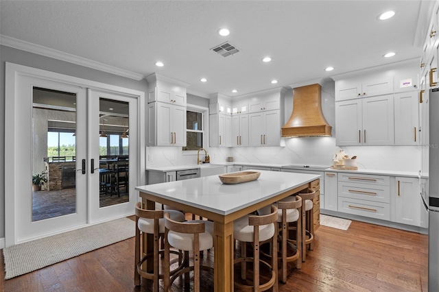 kitchen featuring visible vents, black electric cooktop, custom exhaust hood, and a kitchen bar