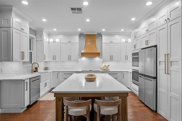 kitchen featuring visible vents, custom exhaust hood, a kitchen island, dark wood-style floors, and appliances with stainless steel finishes