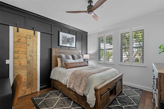 bedroom with a barn door, dark wood finished floors, ornamental molding, and ceiling fan