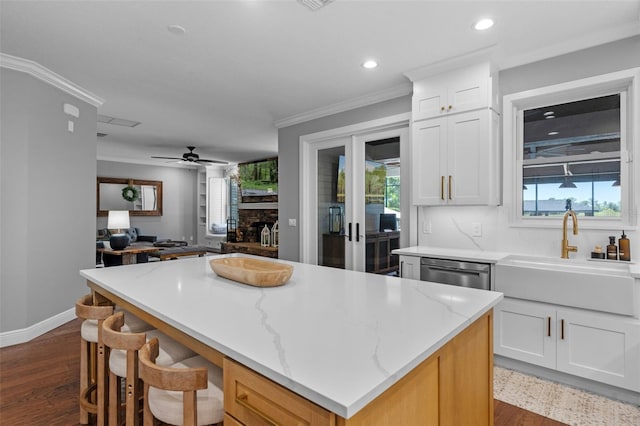 kitchen with a kitchen island, crown molding, stainless steel dishwasher, a fireplace, and a sink