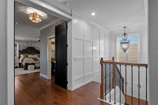 hallway featuring ornamental molding, a decorative wall, dark wood finished floors, and an upstairs landing
