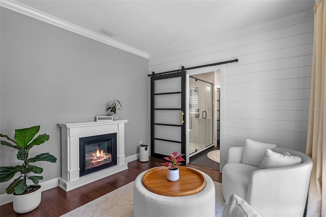 living room with visible vents, ornamental molding, a glass covered fireplace, wood finished floors, and a barn door