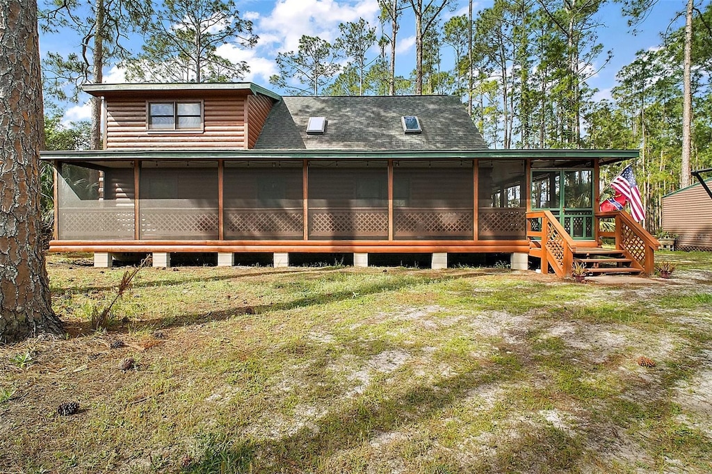 rear view of house featuring a sunroom, a shingled roof, and a lawn