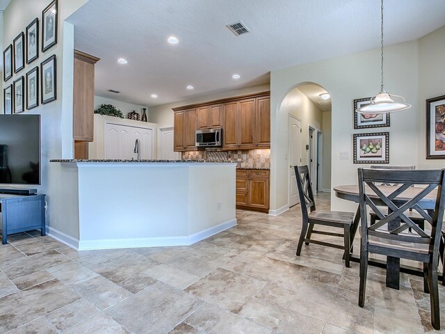 3775 Brantley Place Cir, Apopka, FL 32703 - kitchen with stainless steel microwave, dark stone counters, brown cabinetry, arched walkways, and backsplash