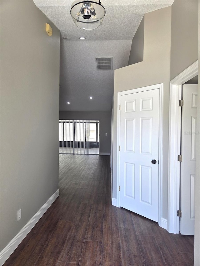 hall with baseboards, dark wood-type flooring, a textured ceiling, and high vaulted ceiling