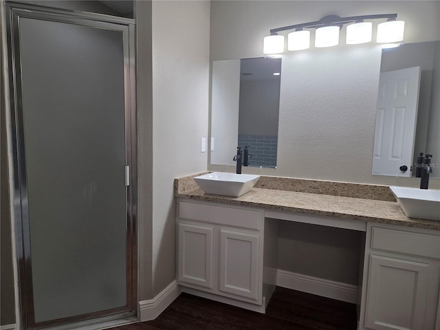 bathroom with a stall shower, wood finished floors, double vanity, and baseboards