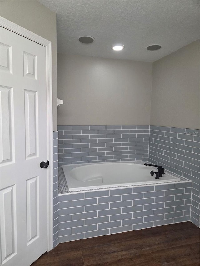 bathroom with a bath, wood finished floors, a textured ceiling, and recessed lighting