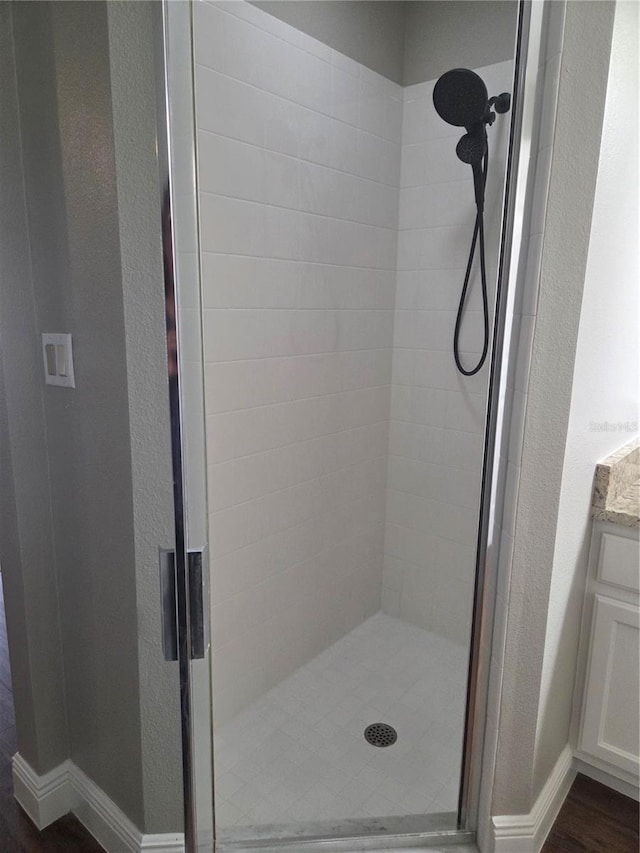 bathroom featuring a stall shower, a textured wall, wood finished floors, vanity, and baseboards