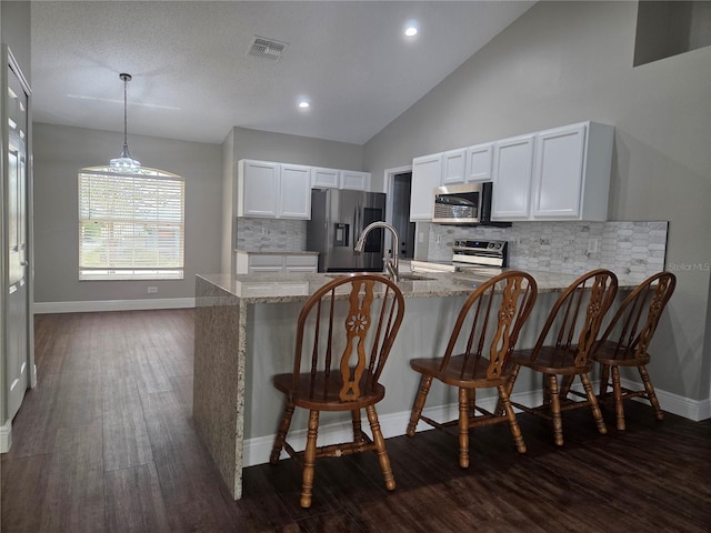 kitchen featuring stainless steel appliances, a peninsula, light stone countertops, white cabinets, and dark wood-type flooring