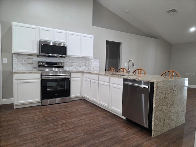 kitchen with appliances with stainless steel finishes, a peninsula, lofted ceiling, decorative backsplash, and white cabinetry