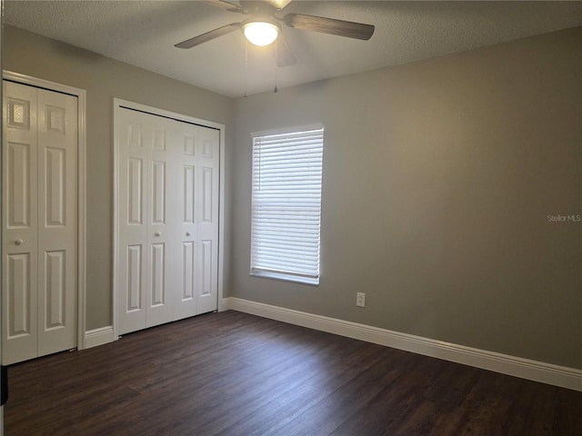 unfurnished bedroom with dark wood-style flooring, baseboards, multiple closets, a textured ceiling, and a ceiling fan