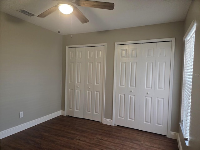 unfurnished bedroom with multiple closets, baseboards, and dark wood finished floors