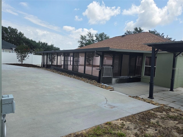 rear view of house featuring a sunroom, fence, a shingled roof, and a patio area