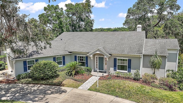 ranch-style house featuring roof with shingles, a chimney, and a front yard