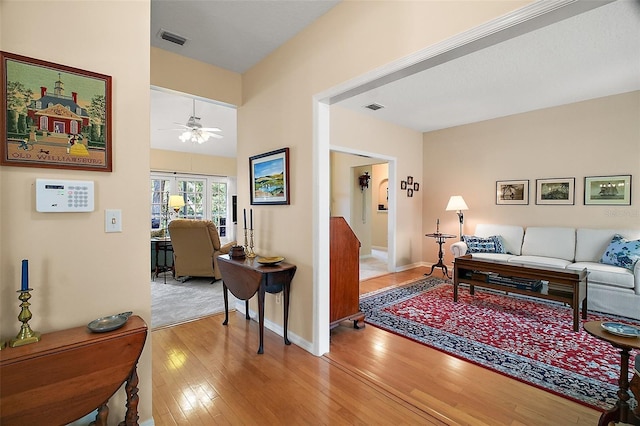 living room featuring baseboards, wood-type flooring, a ceiling fan, and visible vents