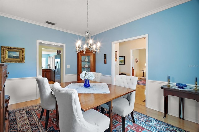 dining room with visible vents, ornamental molding, an inviting chandelier, and light wood-type flooring