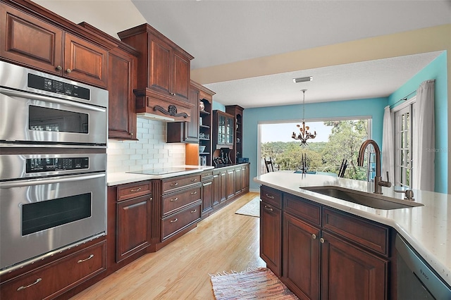 kitchen with decorative backsplash, a sink, light wood-style flooring, appliances with stainless steel finishes, and hanging light fixtures