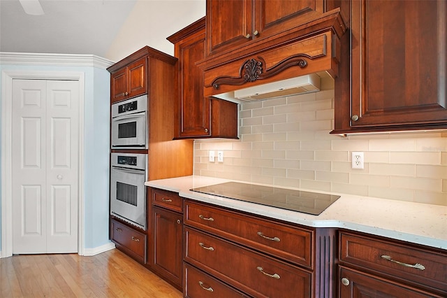 kitchen featuring baseboards, black electric stovetop, light wood finished floors, and tasteful backsplash