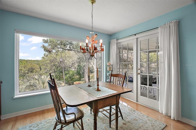 dining space featuring french doors, a textured ceiling, wood finished floors, baseboards, and an inviting chandelier