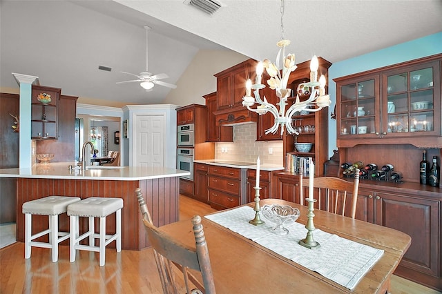 dining area featuring ceiling fan with notable chandelier, vaulted ceiling, light wood finished floors, and visible vents