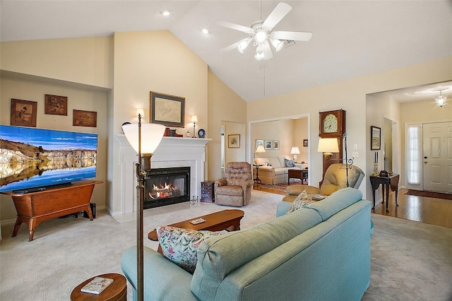carpeted living room with baseboards, a ceiling fan, a glass covered fireplace, and high vaulted ceiling
