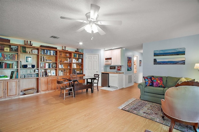 living room featuring light wood-style floors, a ceiling fan, a textured ceiling, and visible vents