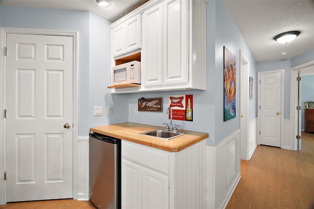 kitchen featuring a textured ceiling, fridge, a sink, white microwave, and light wood finished floors