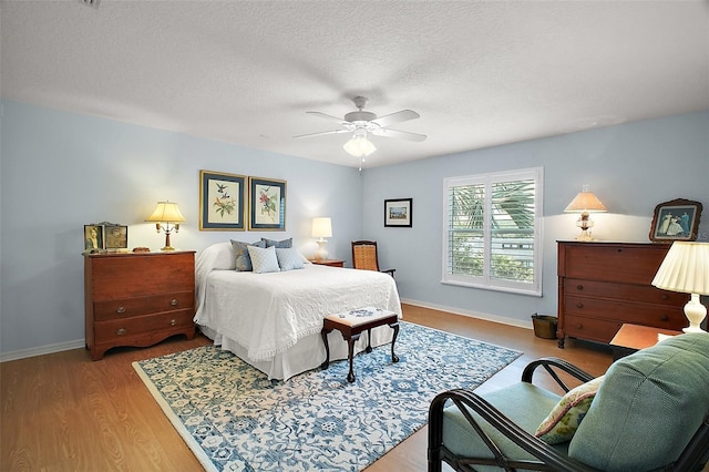 bedroom with baseboards, ceiling fan, a textured ceiling, and wood finished floors