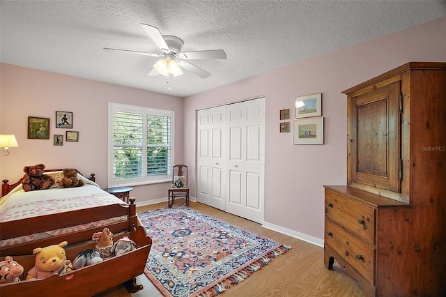 bedroom with light wood-style floors, a textured ceiling, a ceiling fan, baseboards, and a closet