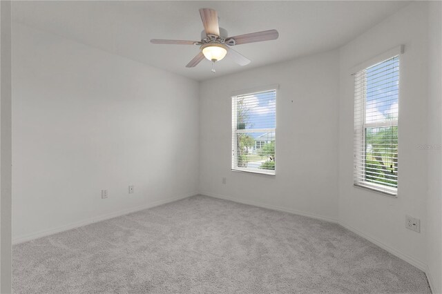 carpeted spare room featuring a healthy amount of sunlight, baseboards, and a ceiling fan