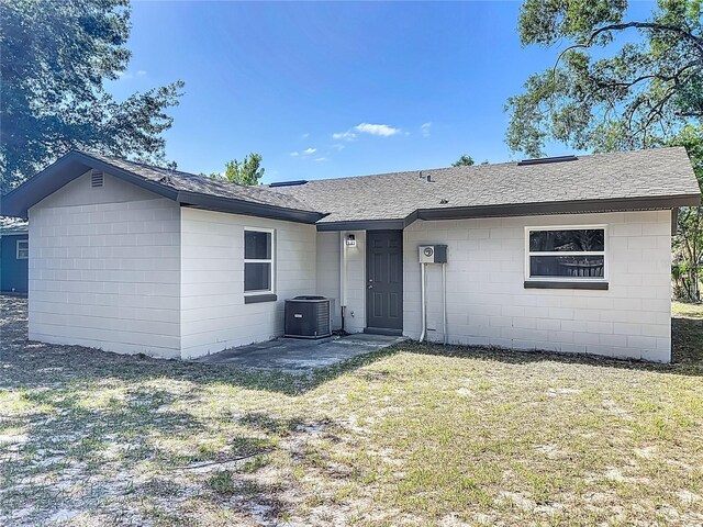 back of house with concrete block siding, a yard, a shingled roof, and cooling unit