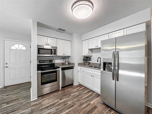 kitchen with appliances with stainless steel finishes, a sink, a textured ceiling, white cabinetry, and visible vents