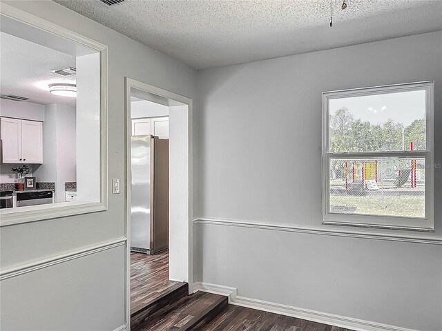 hall with a textured ceiling, visible vents, dark wood-style floors, and baseboards