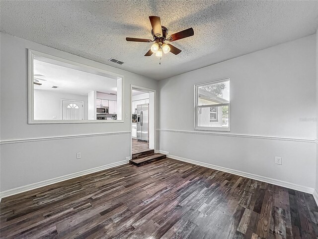spare room featuring baseboards, a ceiling fan, dark wood-style flooring, and a textured ceiling
