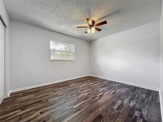 spare room featuring baseboards, ceiling fan, dark wood finished floors, and a textured ceiling