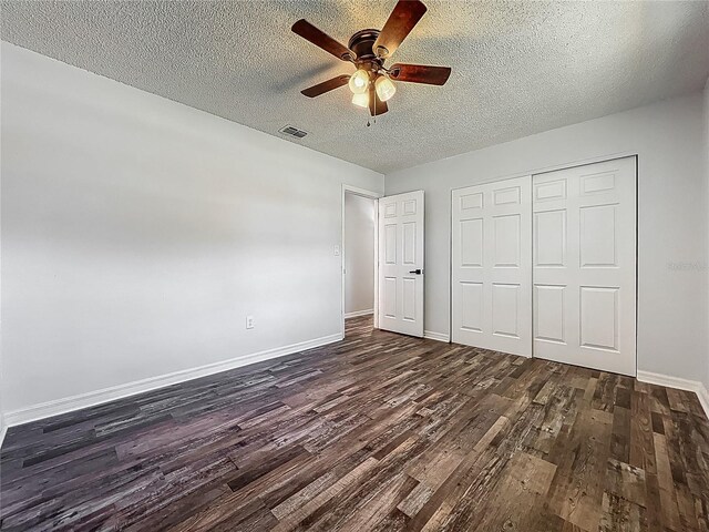 unfurnished bedroom with a textured ceiling, baseboards, visible vents, dark wood-style floors, and a closet