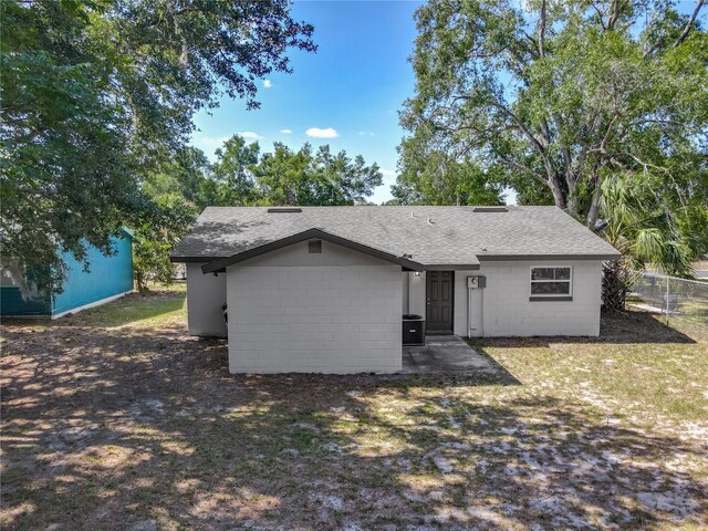back of property with roof with shingles, fence, and concrete block siding
