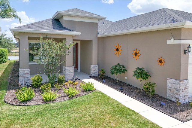 property entrance featuring a shingled roof, stucco siding, a yard, and stone siding