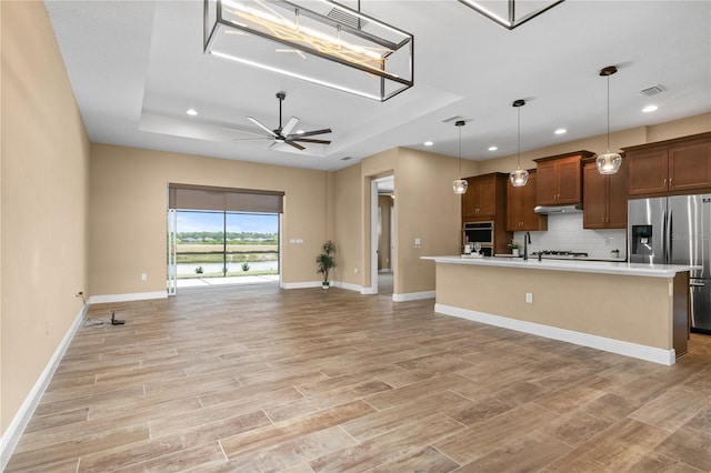 kitchen featuring a raised ceiling, a ceiling fan, open floor plan, backsplash, and stainless steel refrigerator with ice dispenser