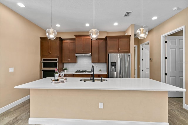 kitchen featuring backsplash, visible vents, stainless steel appliances, a sink, and under cabinet range hood