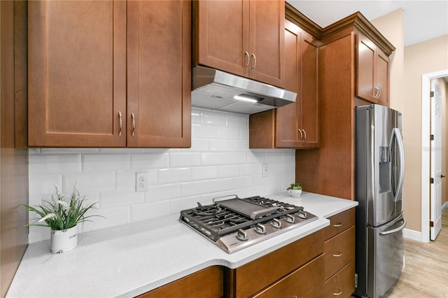 kitchen with decorative backsplash, light wood-style floors, light countertops, under cabinet range hood, and appliances with stainless steel finishes
