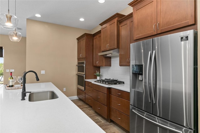 kitchen featuring wood finished floors, a sink, under cabinet range hood, light countertops, and appliances with stainless steel finishes