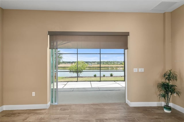 interior space with a water view, wood finished floors, plenty of natural light, visible vents, and baseboards