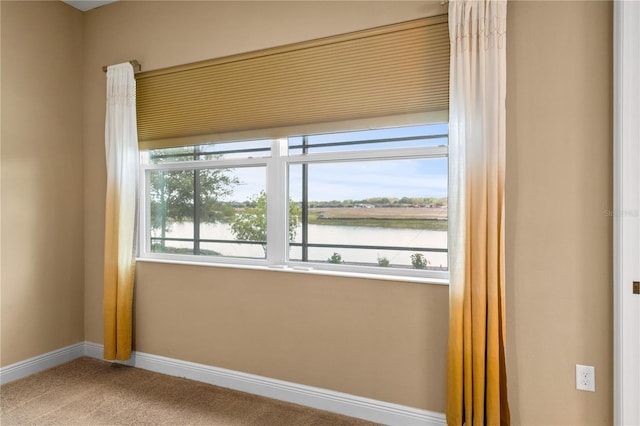 carpeted empty room featuring a water view and baseboards