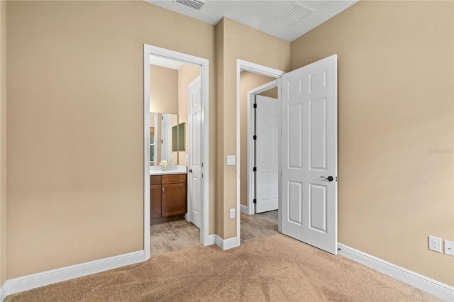 unfurnished bedroom with baseboards, visible vents, ensuite bathroom, and light colored carpet