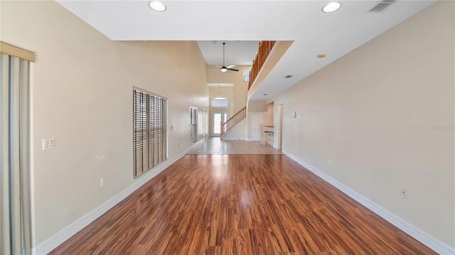 unfurnished room with a ceiling fan, baseboards, visible vents, stairs, and wood finished floors
