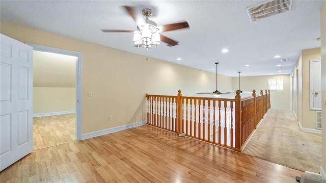 hallway with light wood finished floors, visible vents, and baseboards
