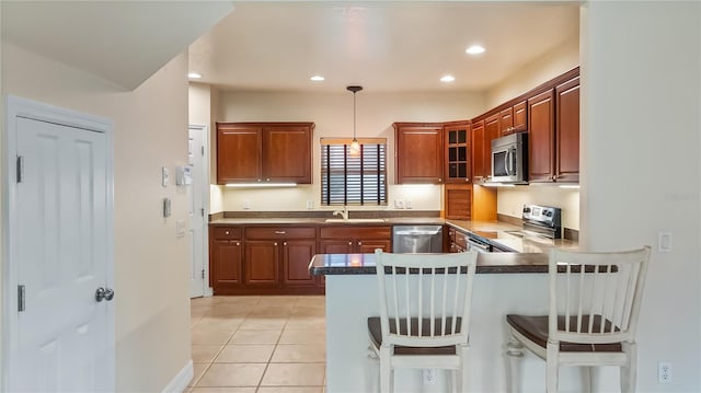 kitchen with a breakfast bar area, glass insert cabinets, a sink, a peninsula, and stainless steel appliances