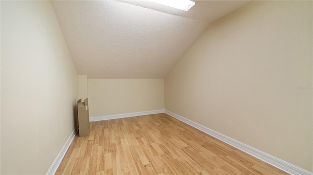 bonus room with light wood-style floors, vaulted ceiling, baseboards, and a textured ceiling